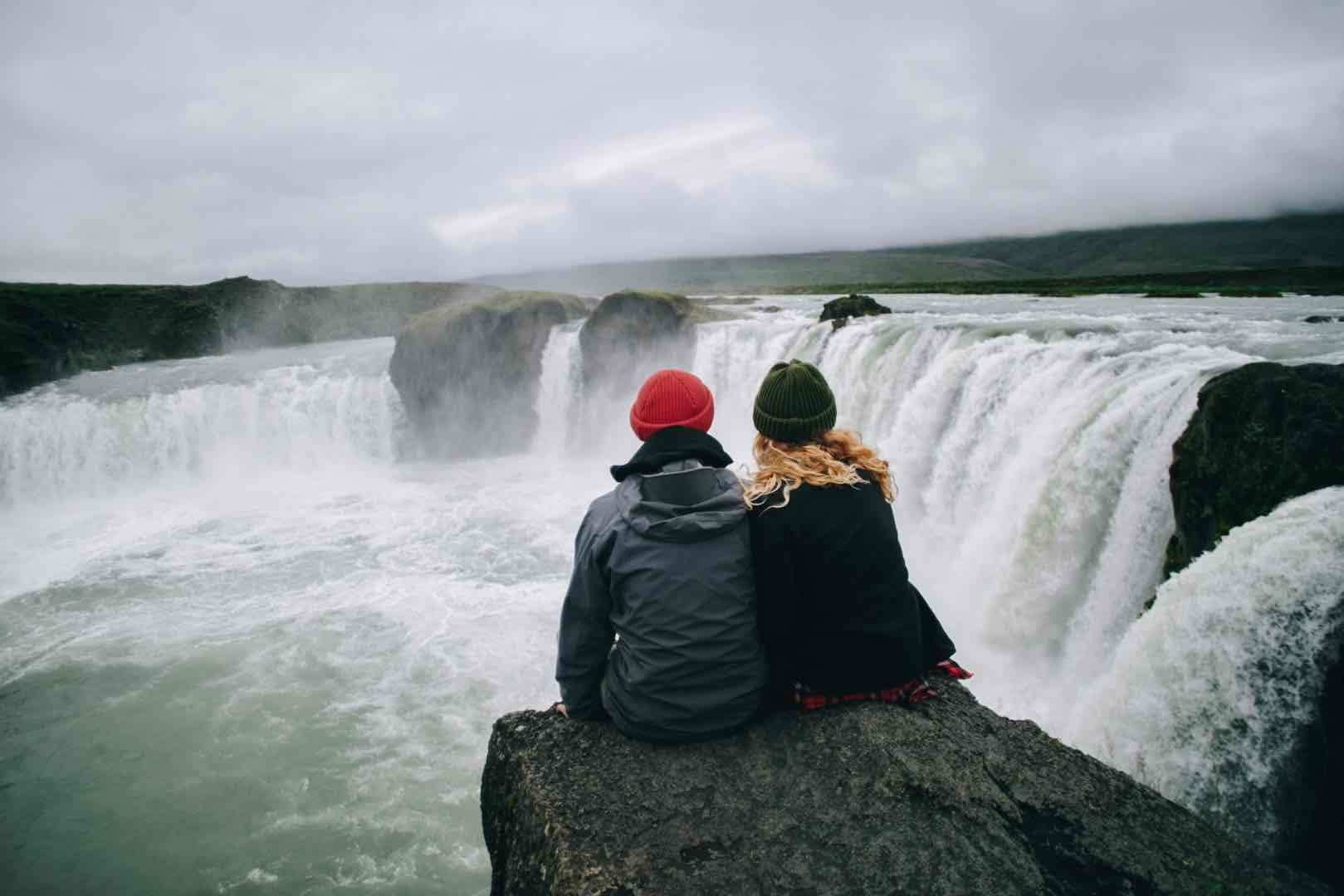 Couple hikers sit over waterfall cliff