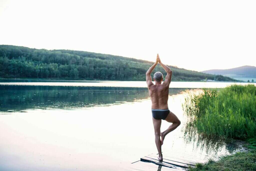 Silhouette of a person in a yoga pose on a wooden pier overlooking a tranquil mountain lake at sunset.